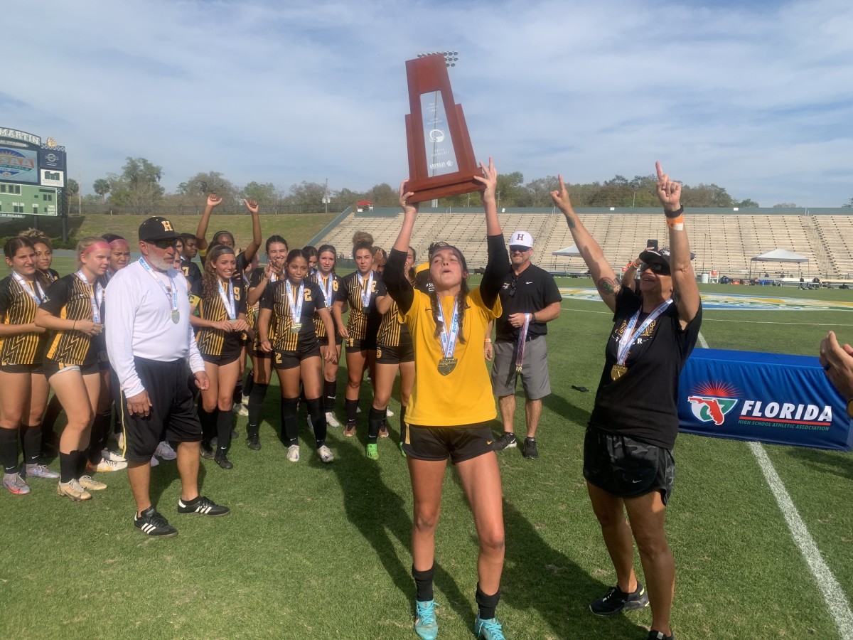 American Heritage goalkeeper Jillian Miliffe lofts up the 5A championship trophy as coach Cindy Marcial and the Patriots celebrate their 0-0 4-2pk win over Mariner.
