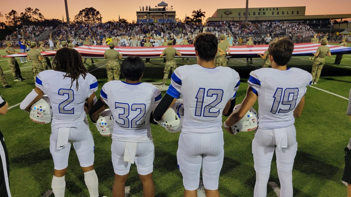 Members of the Barron Collier football team stand at attention, as a large American flag is stretched at midfield, by military personnel, prior to the playing of the national anthem at Naples.