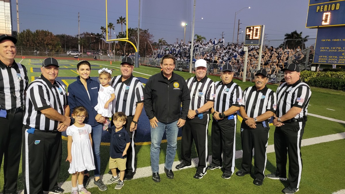 Florida Governor Ron DaSantis, who assisted with the coin toss, is joined by his family in posing for a photo with the game officials, prior to the Naples-Barron Collier contest, Friday at Naples. It marked the return of high school football to the area in the aftermath of Hurricane Ian.