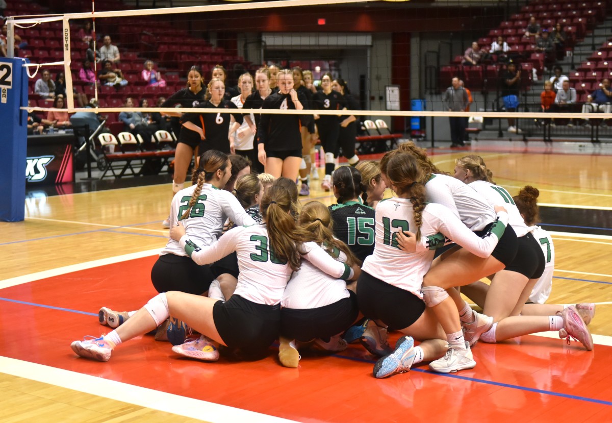 Bishop McGuinness volleyball players dogpile one another on the court after winning the Class 5A state championship Oct. 21, 2023, as Tulsa Booker T. Washington players look on in the background.