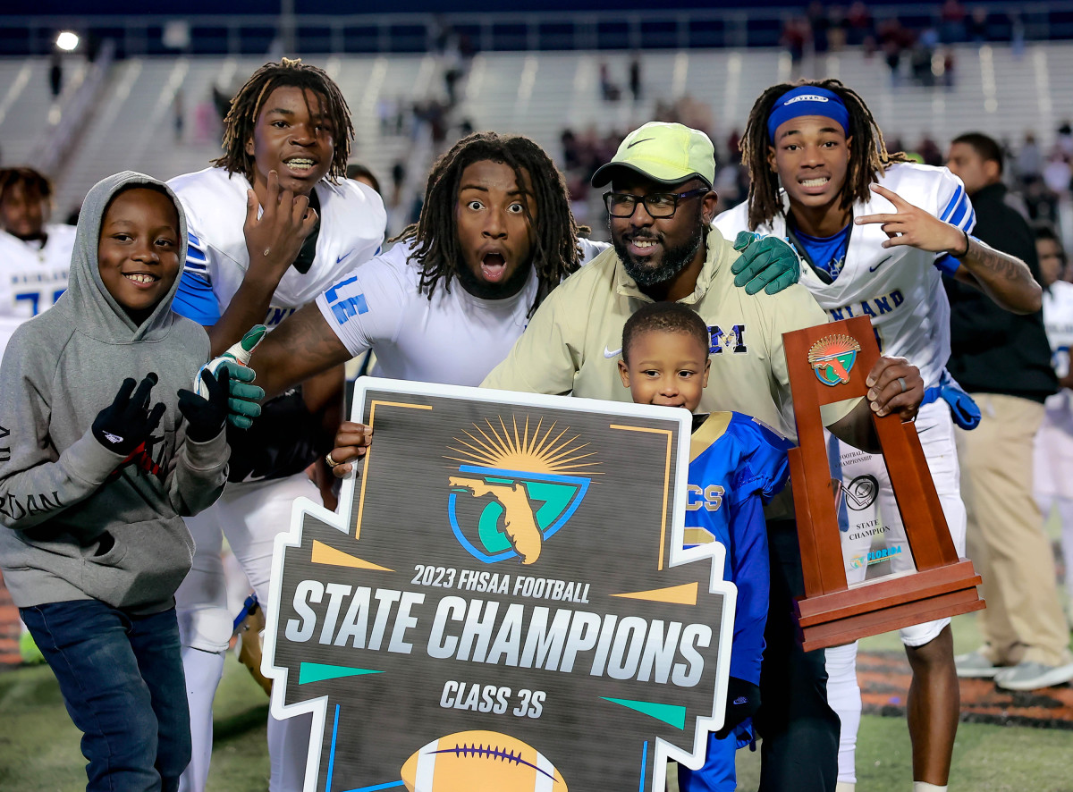 In December, Travis Roland (holding trophy) celebrated winning a state championship with Mainland football team. Soon thereafter he departed Florida to become head coach at Camden County high school in Florida, largely because of better pay and more financial support for football.